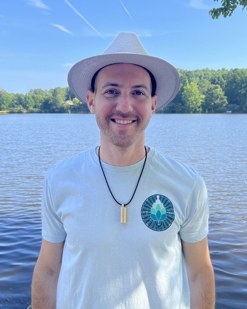 Yoni smiling gently in front of a peaceful lake, reflecting warmth and presence.